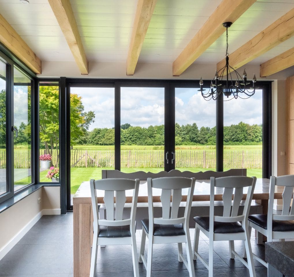 Ruime eetkamer met grote aluminium stalen schuifdeuren naar buiten, modern interieur, natuurlijk licht, uitzicht op tuin en landschap.