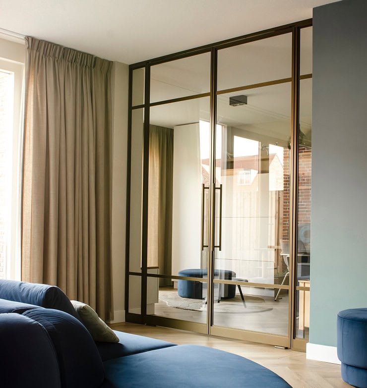 Glazen schuifdeur met metalen frame en gouden handgrepen in moderne woonkamer voor een strakke interieurafwerking.