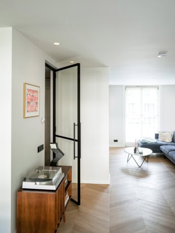 Stalen scheidingsdeur met zwart frame en handvat in een moderne woonkamer, op maat gemaakt door Aluwdoors, voor een strakke en duurzame interieurafwerking.