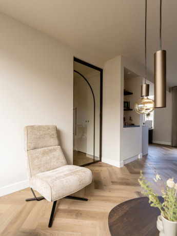 Elegante stalen scheidingsdeur met glas in een modern interieur, gecombineerd met een comfortabele fauteuil en stijlvolle verlichting, perfect voor een eigentijdse woning.