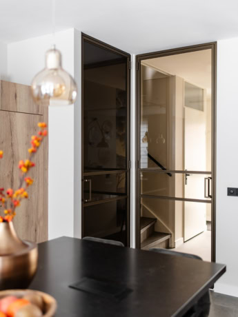 Glazen stalen deuren op maat met zwarte profielen, voorzien van handgrepen, scheiden woonkamer en trapopgang, modern en strak design.