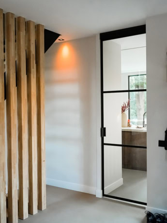 Eenvoudige zwarte stalen schuifdeur tussen woonkamers en keuken met grote ramen voor natuurlijk licht.