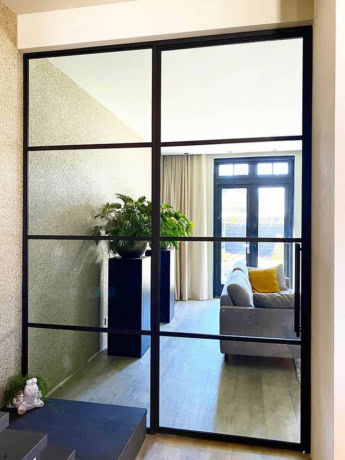 Modern steel sliding door with a black frame and glass panels, ideal for separating living space from an office, made to measure by Aluwdoors.