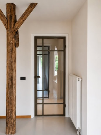 Sleek steel door with stained glass details, perfect for rebated doors, in a bright interior space, combined with a radiator and wooden element.