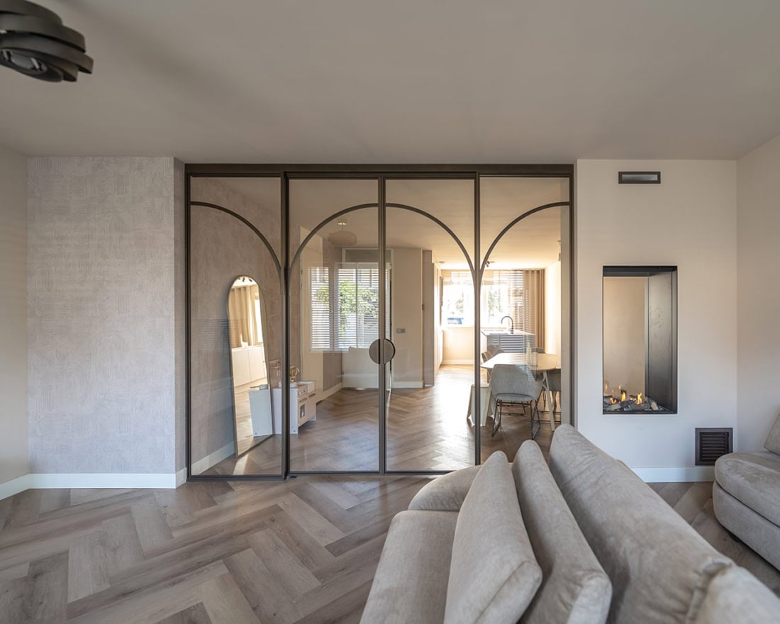 Moderne stalen schuifdeur met glazen panelen in een eigentijdse woonkamer, ideaal voor scheiding van ruimtes en designaccenten, op maat gemaakt door Aluwdoors.