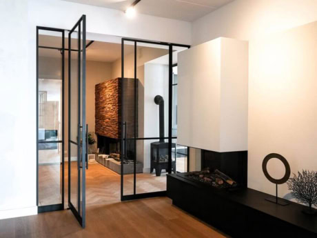 Moderne stalen taatsdeur in woonkamer met zwart frame en glas, scheidt de woonkamer van de hal, passend bij hoogwaardige stalen deuren en wanden op maat.