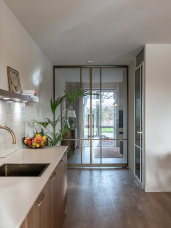 Modern steel pivot door with glass panels, separates the kitchen from the living room and provides an open, light layout in a contemporary interior.