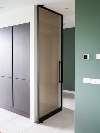 Modern steel pivot door with a black frame and glass, perfect for interior partitioning and design, made to measure by Aluwdoors.