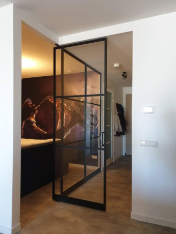 A modern pivot door with a black steel frame and glass, ideal for dividing spaces in a home, made to measure by Aluwdoors.