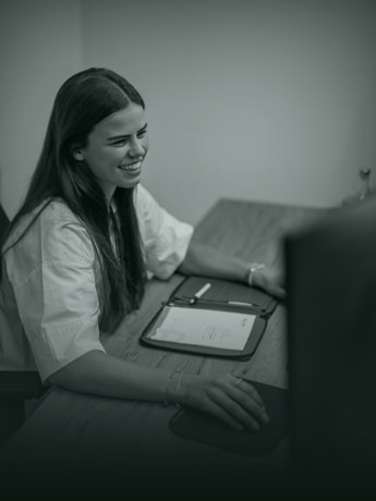 Charmante vrouw werkt op kantoor, glimlachend terwijl ze op haar computer werkt.