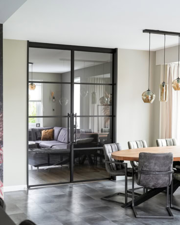 Steel sliding door with black metal frame and glass panels, separate living room and dining area, modern industrial interior style.