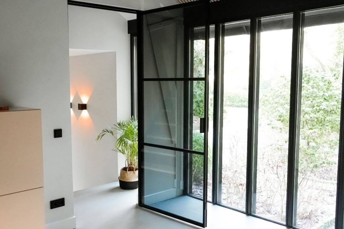 De scharnierdeur inclusief kozijn van Aluwdoors, met daarin het grijze glas.