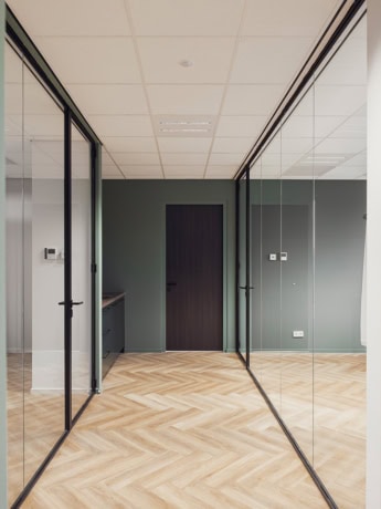 Glaswand met zwarte stalen deuren in een modern kantoor met houten vloer.