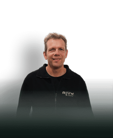 Een man in een zwarte jas met ALUW logo die trots naast een stalen deur staat, voor hoogwaardige stalen deuren en wanden op maat.
