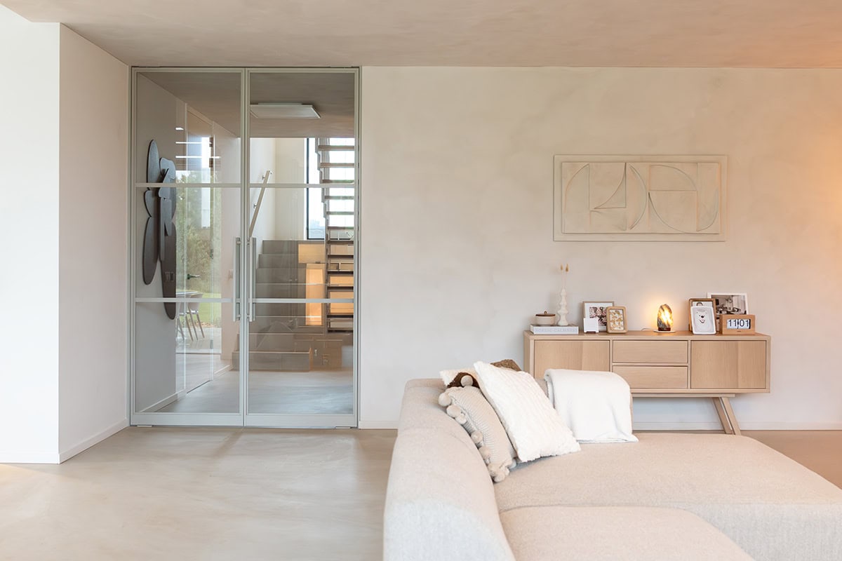Strakke stalen schuifdeur met glazen panelen in een moderne, minimalistische woonkamer met neutral kleuren.