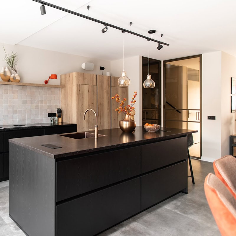 Strakke zwarte keukeneiland met fijn betonlook vloer en natuurlijke houten kasten op maat, modern interieur met sfeervol licht en decoratie.