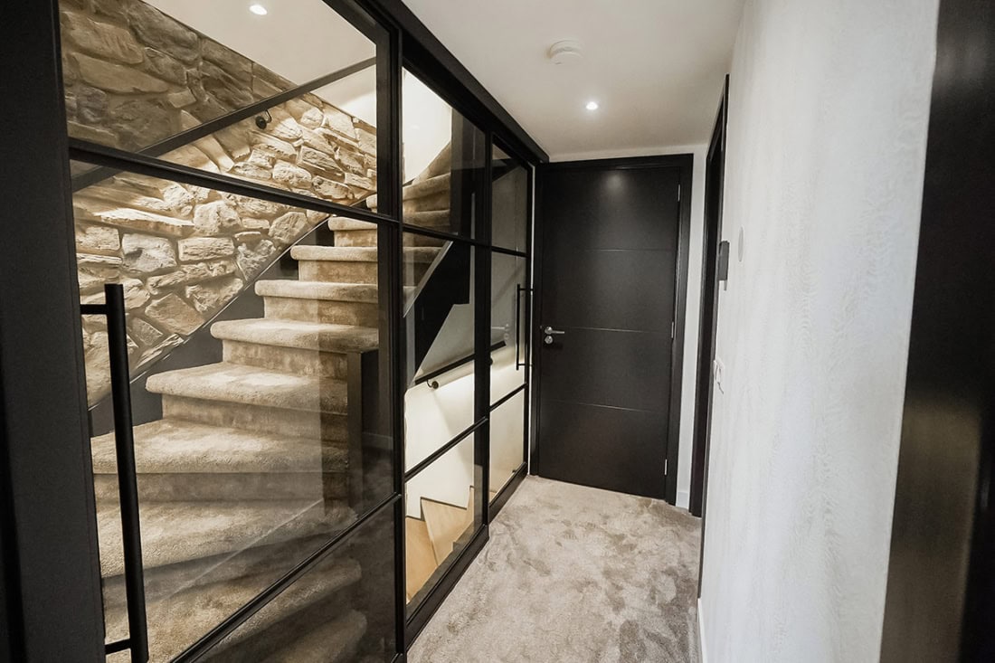 Strakke stalen deur met glas en zwarte frame in modern interieur bij trap en betonwand.