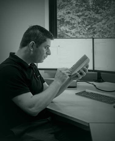 Binnenkantoor medewerker controleert technische specificaties op een tablet met twee monitors op de achtergrond, afgestemd op hoogwaardige stalen deuren en maatwerk wanden.