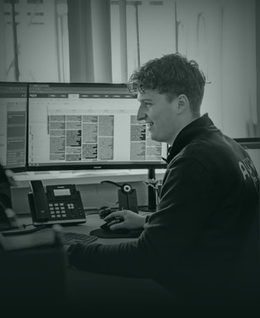 Software engineer werkt aan bedrijfssoftware op kantoor met meerdere beeldschermen.