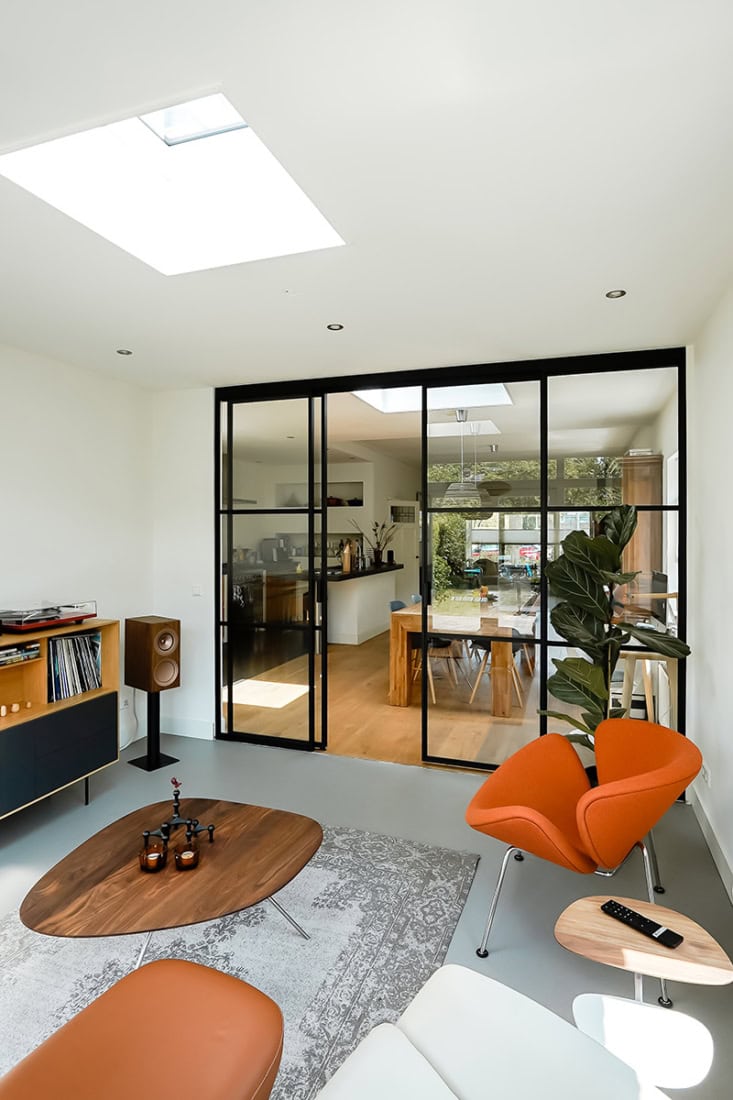 Glazen stalen scheidingswand met zwarte profielafwerking en grote raampartijen in een modern ingerichte woonkamer.