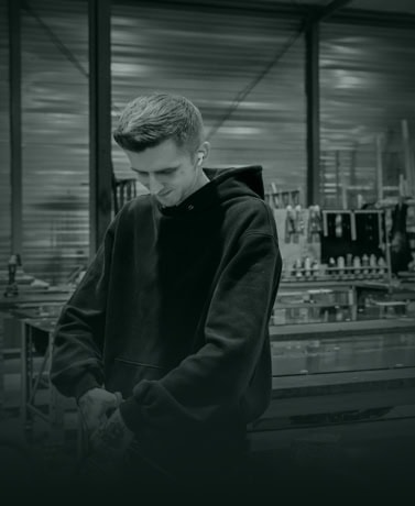 Moderne jonge man in een werkplaats met staal, met een hoodie, bezig met constructiewerk of metaalbewerking in een industriële omgeving.