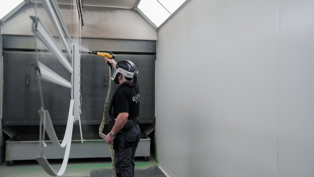 Een man die een stalen deur schoonmaakt met een hogedrukreiniger in een hoge, lichte ruimte.