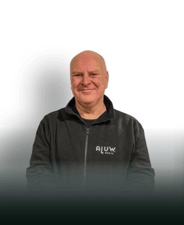 Een man in een zwart ALUW-deurbroek, die trots voor een witte achtergrond staat, vertegenwoordigt kwaliteit en maatwerk in stalen deuren en wanden van ALUWdoors.