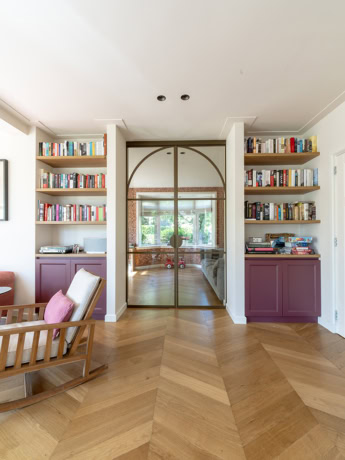 Moderne stalen deur met glazen panelen, omgeven door ingebouwde boekenkasten, in een lichte en ruime woonkamer, perfect voor een stijlvolle en functionele indeling.