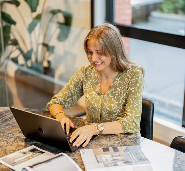Inkoopmedewerker werkt aan laptop met documenten en notities, klaar voor het maken van inkoopbeslissingen. Professionele werkplek voor efficiënte inkoopprocessen.