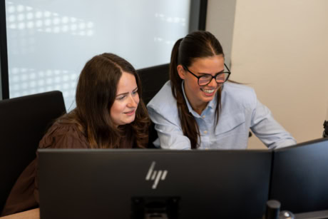 Twee vrouwen werken samen aan een computer, met een focus op hoogwaardige stalen deuren en wanden op maat, passend bij de diensten van Aluwdoors.